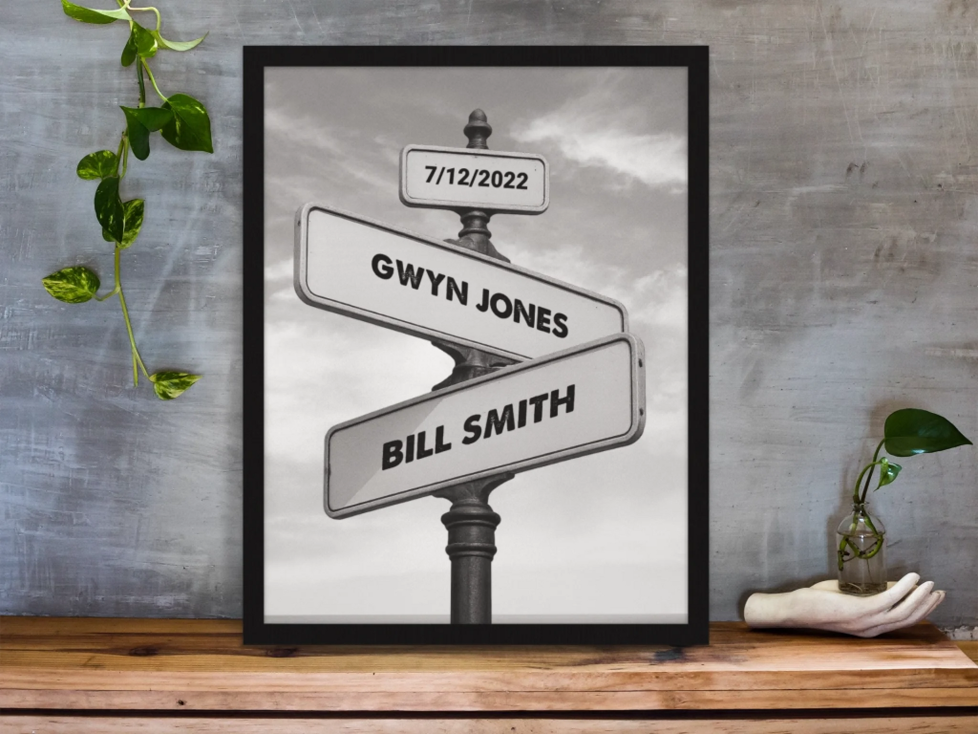 framed-art-print-standing-on-a-wooden-desk-against-a-concrete-wall-near-a-hand-decoration-a10403